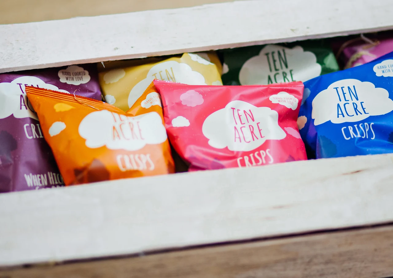 Colourful Ten Acre crisp packets displayed inside a white wooden crate.